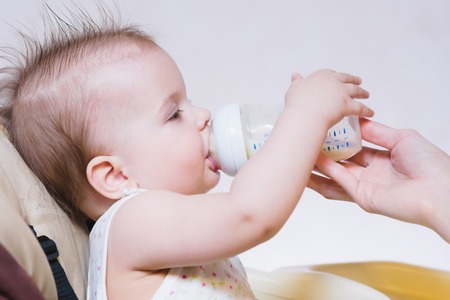 woman gives to drink baby milk in the houseの写真素材