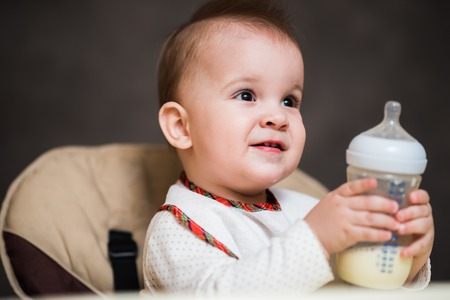 baby drinks from a bottle of milk in the house