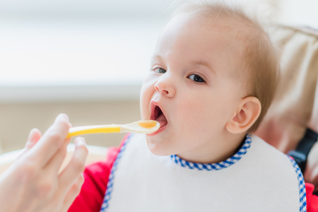 small child sits on a chair and eating with spoonの写真素材