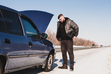 man stands near his broken car in winterの写真素材