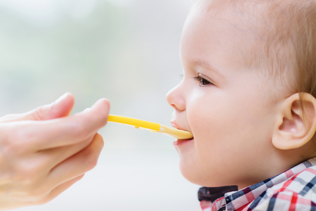 small child sits on a chair and eating with spoonの写真素材