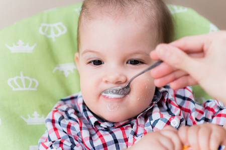 small child sits on a chair and eating with spoonの写真素材