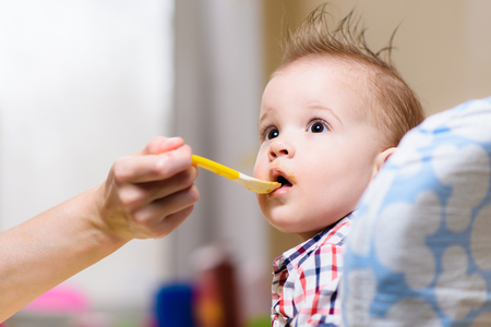 small child sits on a chair and eating with spoonの写真素材