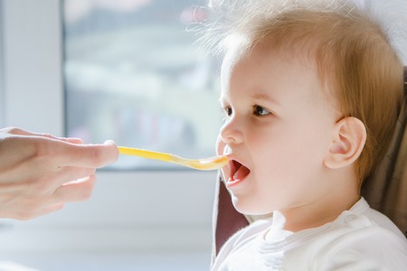 small child sits on a chair and eating with spoonの写真素材