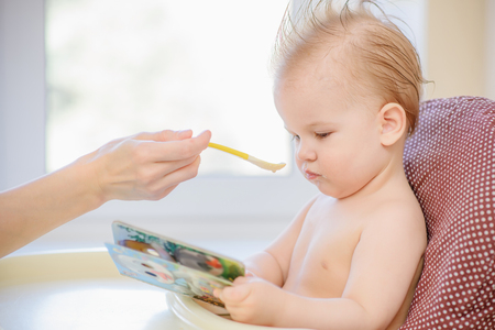small child sits on a chair and eating with spoonの写真素材