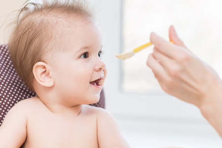 small child sits on a chair and eating with spoonの写真素材