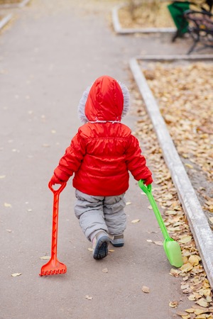 A small child with a rake and a shovel walks in the parkの写真素材