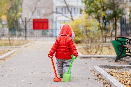 A small child with a rake and a shovel walks in the parkの写真素材