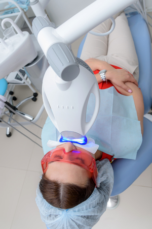 the girl undergoes the procedure of teeth whitening with the help of ultraviolet lampの写真素材