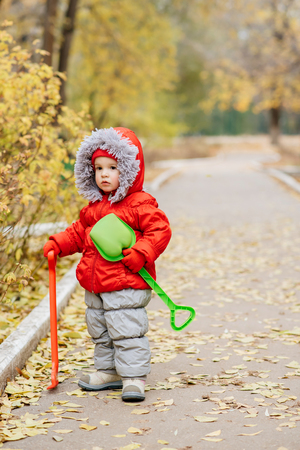 A small child with a rake and a shovel walks in the parkの写真素材