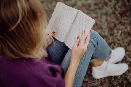 Girl reading a book sitting on the grass in the parkの写真素材