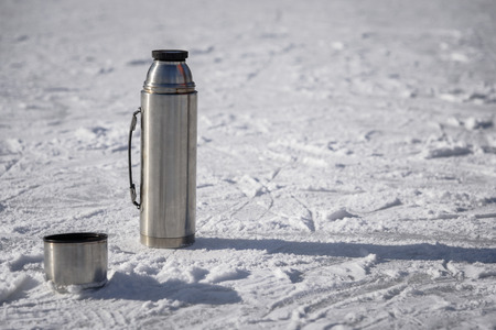an open vacuum flask stands on ice with a cup of hot teaの写真素材