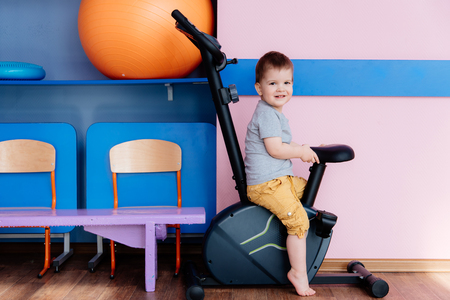 little kid sits on an exercise bike in the gymの写真素材
