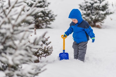 A little boy is digging snow with a shovel in the winter outside.の写真素材