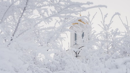 white Orthodox church with a golden dome on the background of branches with hoarfrostの写真素材