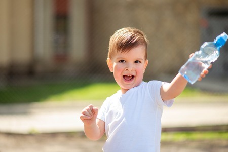 cool baby drinks clean water from a bottle on a sunny day in natureの写真素材
