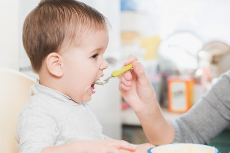 mom in the kitchen is feeding the baby porridgeの写真素材