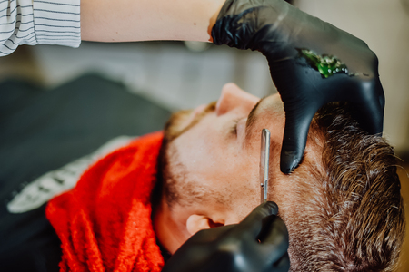 the barber shaves his beard with a man with a razorの写真素材