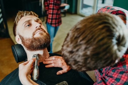 young guy hairdresser cuts beard to man in salonの写真素材