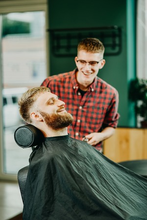 young guy hairdresser cuts beard to man in salon