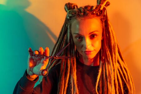 woman hairdresser with dreadlocks holding scissors in hand close-upの写真素材