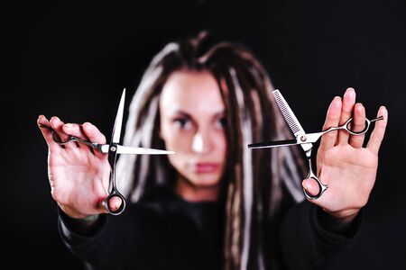 woman hairdresser with dreadlocks holding scissors in hand close-upの写真素材