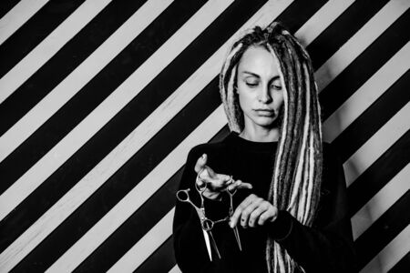 woman hairdresser with dreadlocks holding scissors in hand close-up