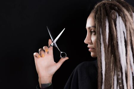 woman hairdresser with dreadlocks holding scissors in hand close-upの写真素材