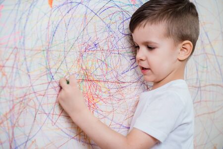 The child draws on the wall with colored chalk. The boy is engaged in creativity at home