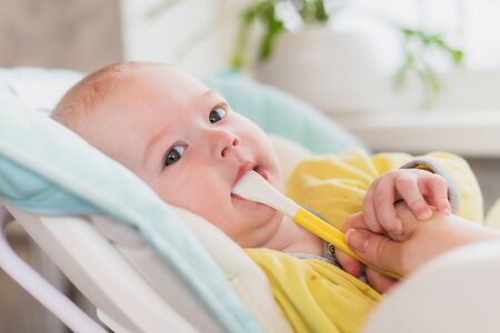 Mom feeds baby vegetable puree in a high chair. The mother puts a spoon of mashed in the child's...