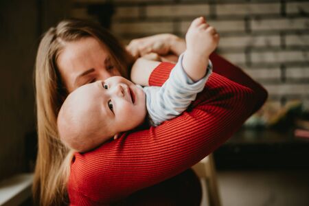 A mom holds a child in her arms. A mother kisses a toddler. A young women hugs her infant. A girl has fun and rejoices with the baby.の写真素材