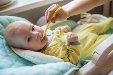 Mom feeds baby vegetable puree in a high chair. The mother puts a spoon of mashed in the child's...