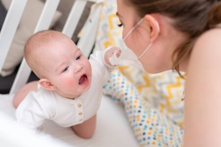 A woman in a medical protective mask takes care of her baby. Prophylactic protection of coronavirus...