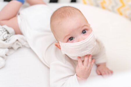 A newborn baby in a medical mask lies in quarantine at home during the coronavirus and covid-19 pandemic.の写真素材