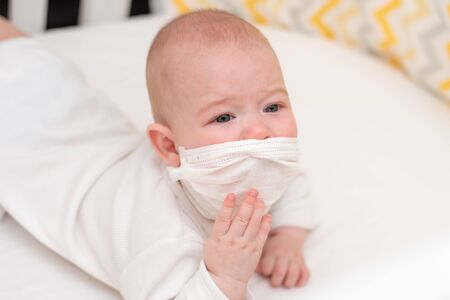 A newborn baby in a medical mask lies in quarantine at home during the coronavirus and covid-19 pandemic.の写真素材