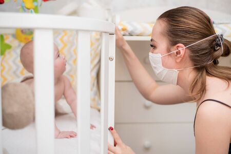 Prevention of the epidemic of coronavirus and covid-19. A woman in a protective mask looks after a newborn baby who is in quarantine at homeの写真素材