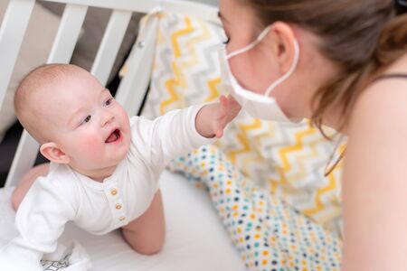 A woman in a medical protective mask takes care of her baby. Prophylactic protection of coronavirus and covid-19 during a pandemic.の写真素材