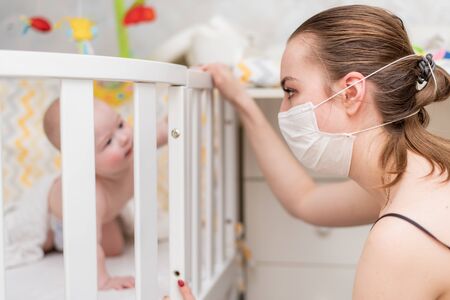 Prevention of the epidemic of coronavirus and covid-19. A woman in a protective mask looks after a newborn baby who is in quarantine at homeの写真素材