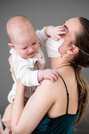 A mother in a protective mask with a baby is sitting at home in quarantine during the coronovirus...