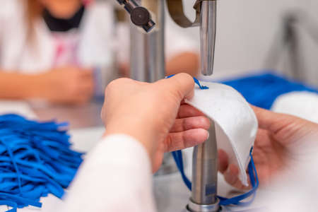 Girls work at the machine for the manufacture of medical masks with nanofibre and solder the loops...