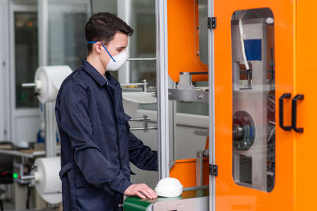 The guy works in a factory for the manufacture of medical masks with nanofiber. Coronovirus and Covid-19 Protectionの写真素材