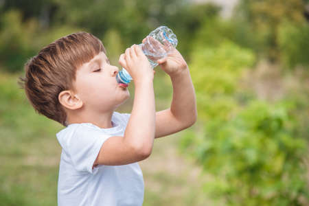 Handsome boy drinks clean water from a bottle on the street in summerの写真素材