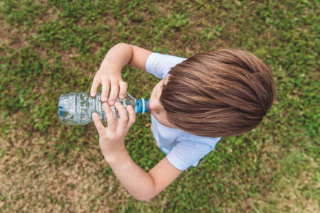 Handsome boy drinks clean water from a bottle on the street in summerの写真素材