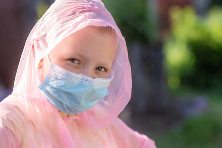 Portrait of a girl in a protective suit and a medical mask on the street in summer. Prevention against coronavirus and Covid-19 during a pandemicの写真素材