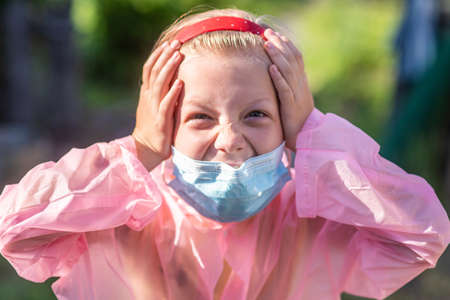 Portrait of a frightened child in protective clothing and a medical mask on the street in summer. Prevention of coronavirus and Covid-19 during a pandemicの写真素材