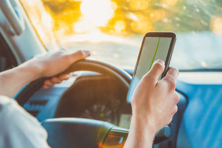 A tourist is sitting in a car and looking for the road in the Navigator app on a Sunny day