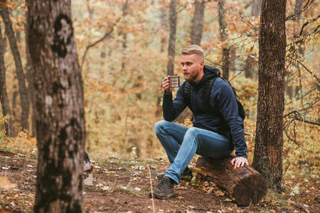 Guy traveler in the autumn forest rests on a halt and drinks tea.
