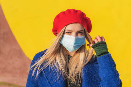 Beautiful woman in a medical mask on a yellow background. Covid-19 coronavirus pandemic concept. Protection against the SARS-CoV-2 virusの写真素材