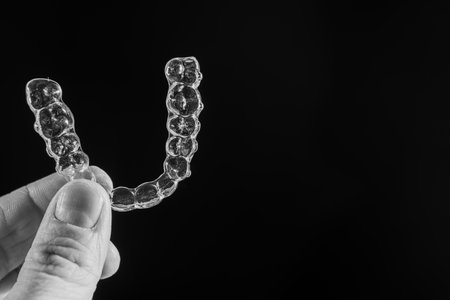 The guy holds in his hand transparent aligners plastic braces retainers for straightening teeth on a...