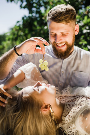 Happy couple spend time together and feed each other grapes in summer on a sunny dayの写真素材